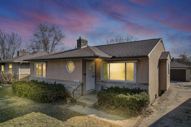 single story home featuring stucco siding, an outbuilding, a chimney, and a shingled roof