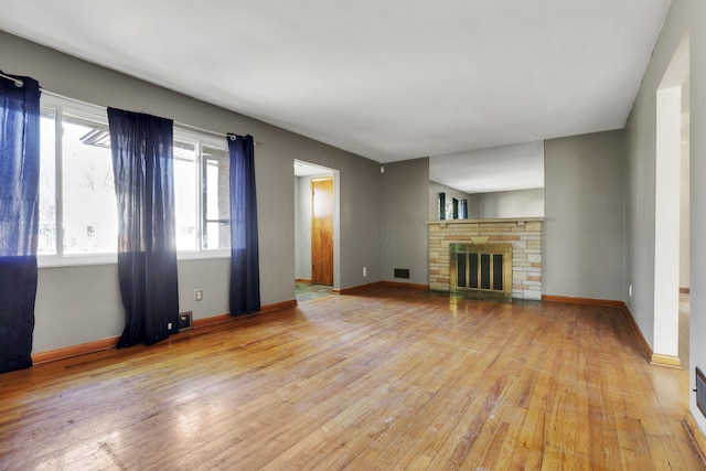 unfurnished living room with a stone fireplace, visible vents, light wood-type flooring, and baseboards