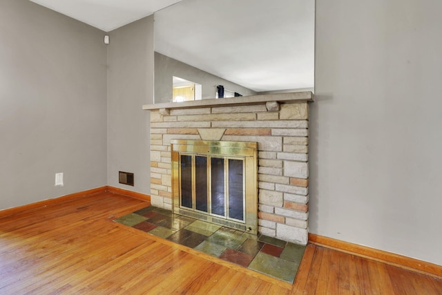 details featuring a stone fireplace, wood finished floors, visible vents, and baseboards