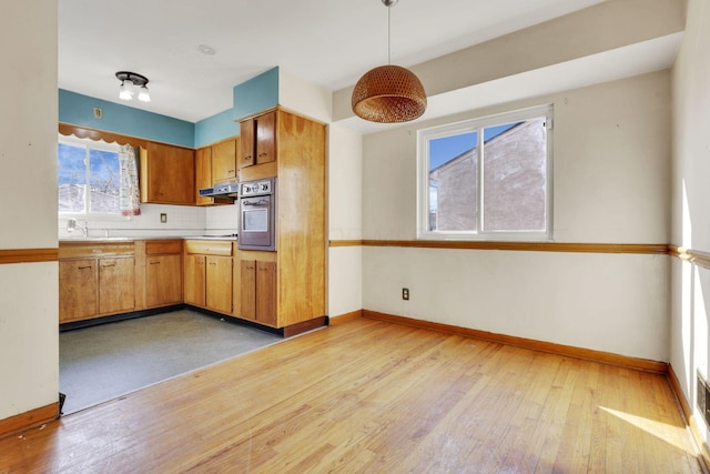 kitchen with light wood-style flooring, backsplash, light countertops, stainless steel oven, and baseboards