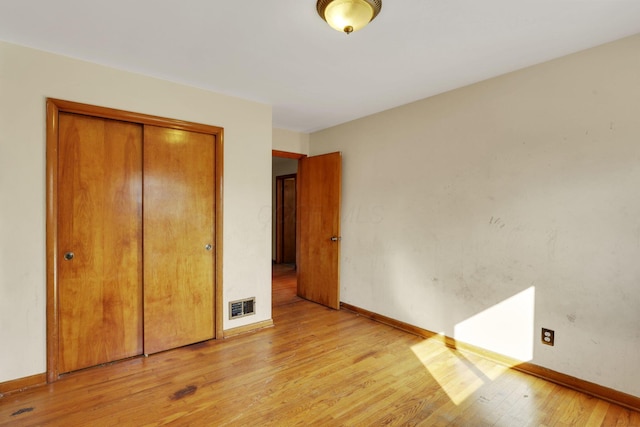 unfurnished bedroom with light wood-type flooring, visible vents, baseboards, and a closet