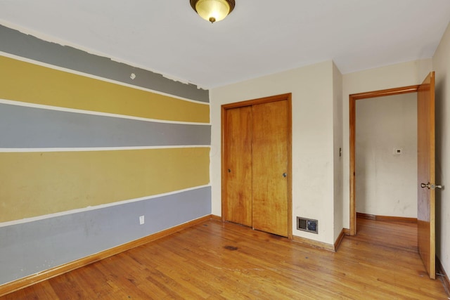 unfurnished bedroom featuring visible vents, wood finished floors, a closet, and baseboards