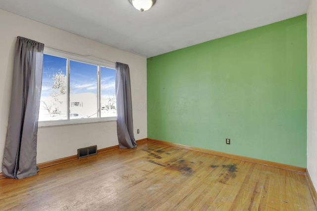 unfurnished room featuring visible vents, baseboards, and hardwood / wood-style floors