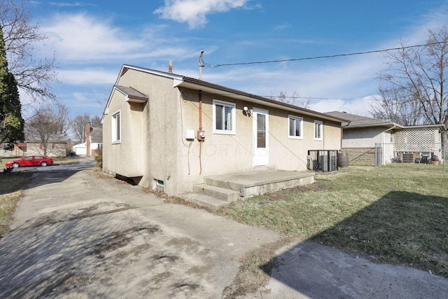 rear view of house with stucco siding, a lawn, fence, concrete driveway, and central AC unit