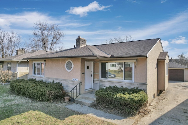 view of front of property featuring stucco siding, a chimney, an outdoor structure, and a shingled roof