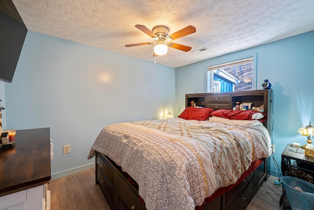 bedroom with visible vents, baseboards, ceiling fan, wood finished floors, and a textured ceiling