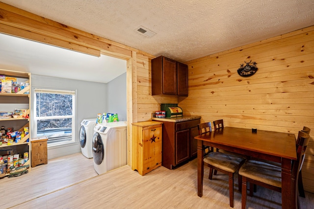 laundry area featuring wooden walls, visible vents, light wood-style floors, a textured ceiling, and washer and clothes dryer