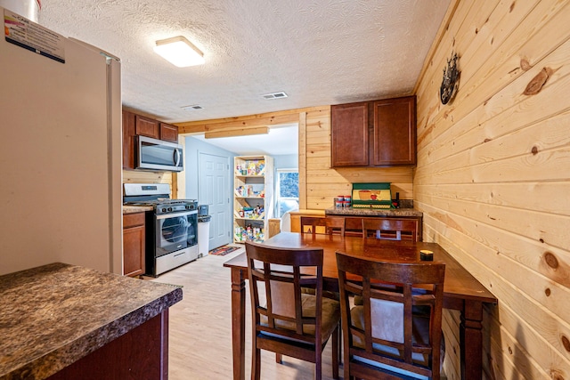 kitchen featuring dark countertops, visible vents, wood walls, light wood-style flooring, and stainless steel appliances