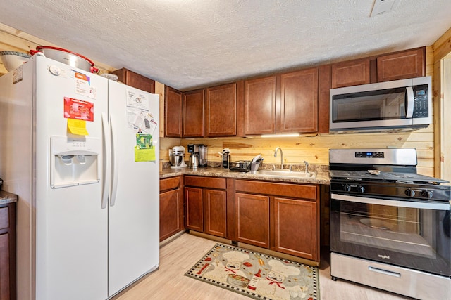 kitchen with a sink, a textured ceiling, appliances with stainless steel finishes, and light wood-style flooring