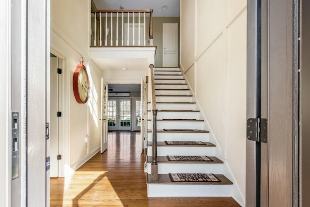 foyer featuring baseboards, wood finished floors, stairs, a high ceiling, and french doors