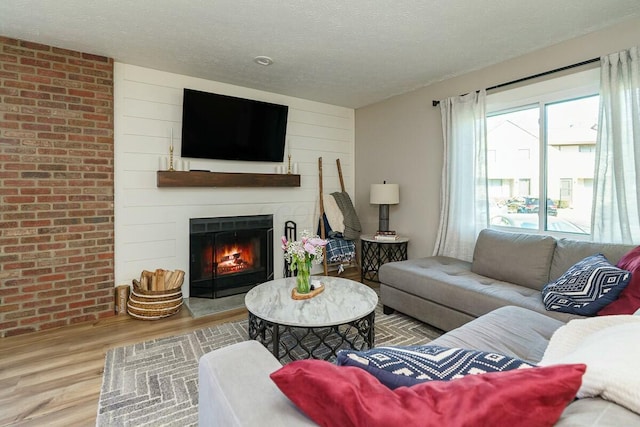 living room featuring a large fireplace, wooden walls, wood finished floors, and a textured ceiling