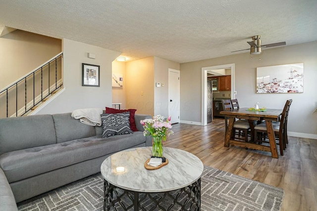 living area with a ceiling fan, wood finished floors, baseboards, stairs, and a textured ceiling