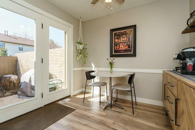 dining area featuring visible vents, baseboards, ceiling fan, light wood-style floors, and a textured ceiling