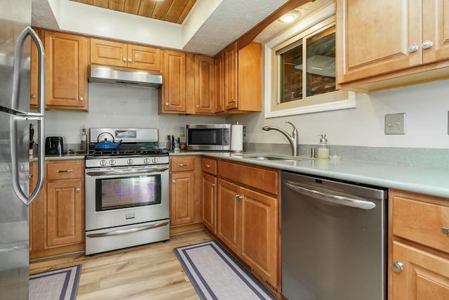 kitchen featuring under cabinet range hood, brown cabinets, appliances with stainless steel finishes, light wood-style floors, and a sink