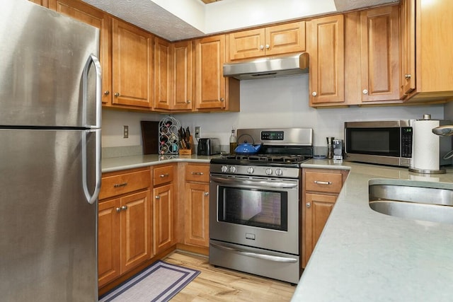 kitchen with under cabinet range hood, stainless steel appliances, and light countertops