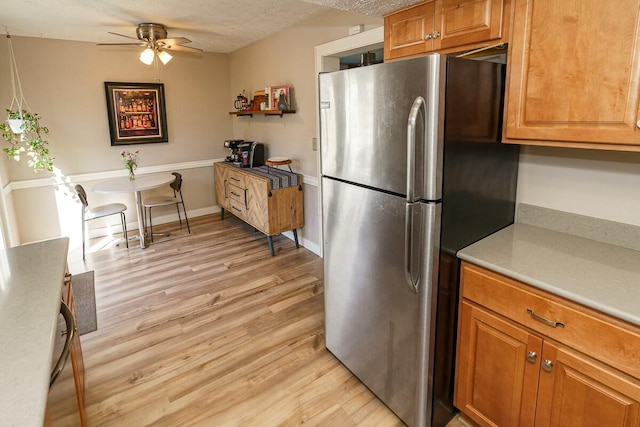 kitchen featuring brown cabinetry, freestanding refrigerator, light countertops, a textured ceiling, and light wood-type flooring