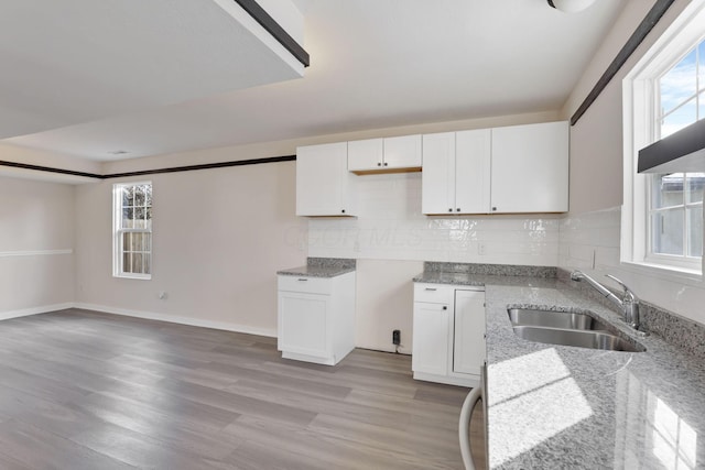 kitchen featuring light stone counters, decorative backsplash, white cabinets, a sink, and light wood-type flooring