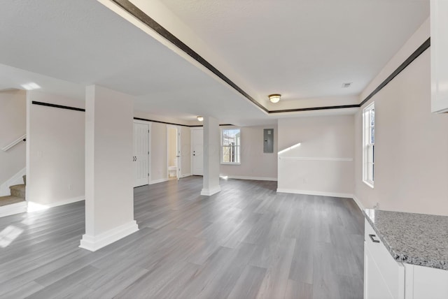 unfurnished living room with light wood-style floors, baseboards, electric panel, and stairway