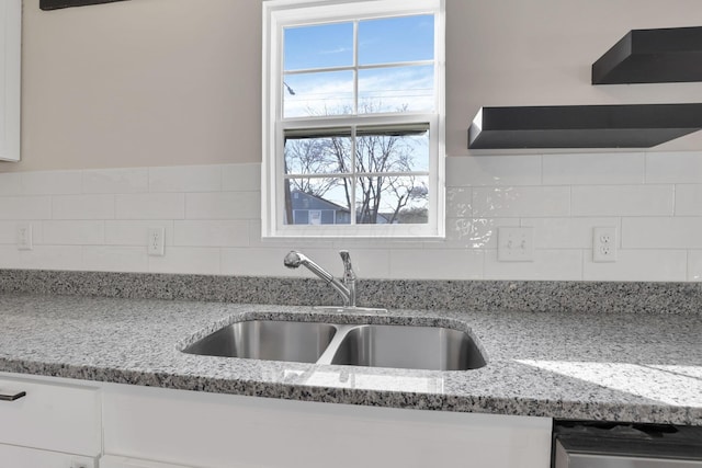 kitchen with light stone counters, white cabinets, a sink, and backsplash