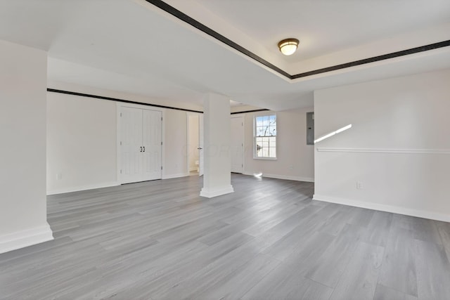 unfurnished living room featuring wood finished floors, a raised ceiling, electric panel, and baseboards