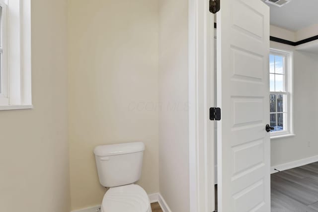 bathroom with toilet, visible vents, baseboards, and wood finished floors