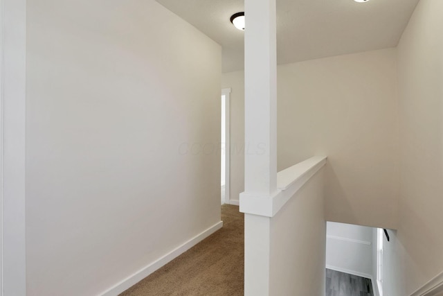 corridor with carpet floors, baseboards, and an upstairs landing