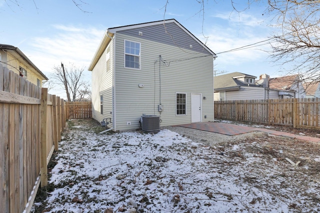 snow covered back of property with cooling unit, a patio area, and a fenced backyard