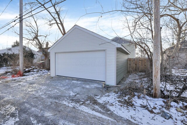 snow covered garage with a detached garage and fence