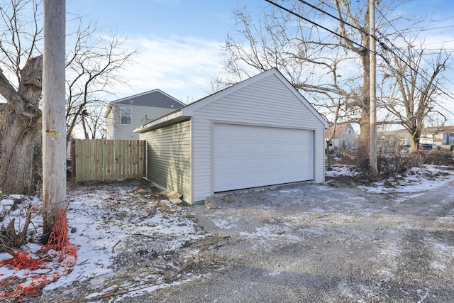 snow covered garage featuring a detached garage and fence