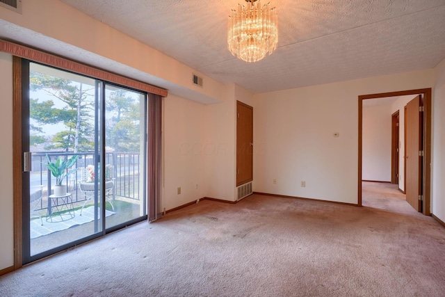 spare room with light carpet, a textured ceiling, visible vents, and a notable chandelier