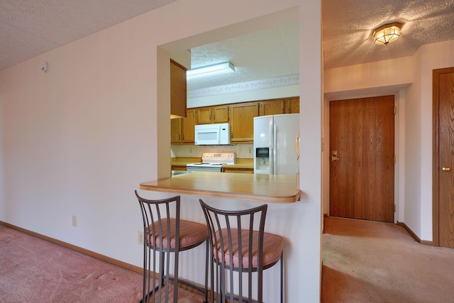 kitchen featuring a textured ceiling, white appliances, carpet, and a kitchen breakfast bar