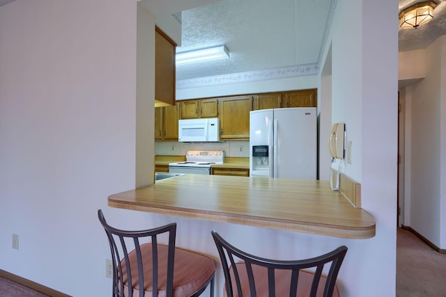 kitchen with white appliances, a breakfast bar area, a peninsula, a textured ceiling, and carpet floors