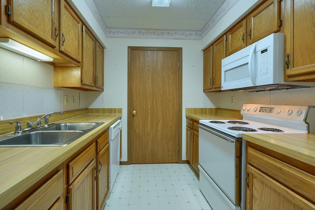 kitchen with brown cabinets, light floors, a sink, a textured ceiling, and white appliances