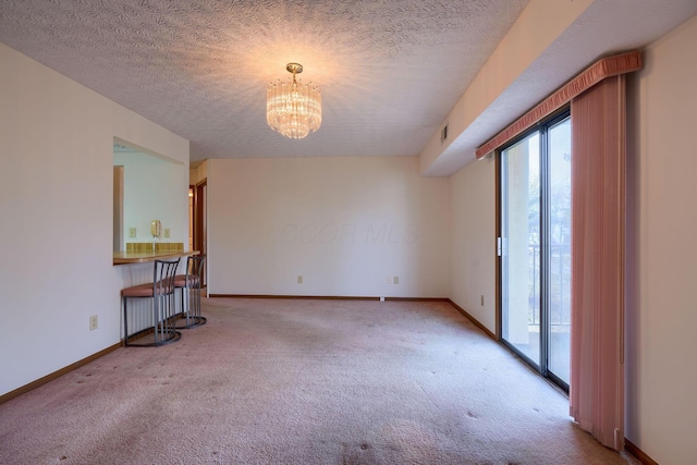 unfurnished room featuring carpet, a textured ceiling, a chandelier, and baseboards