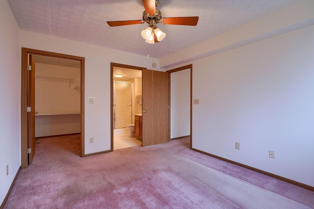 unfurnished bedroom with a textured ceiling, light carpet, baseboards, a spacious closet, and a closet