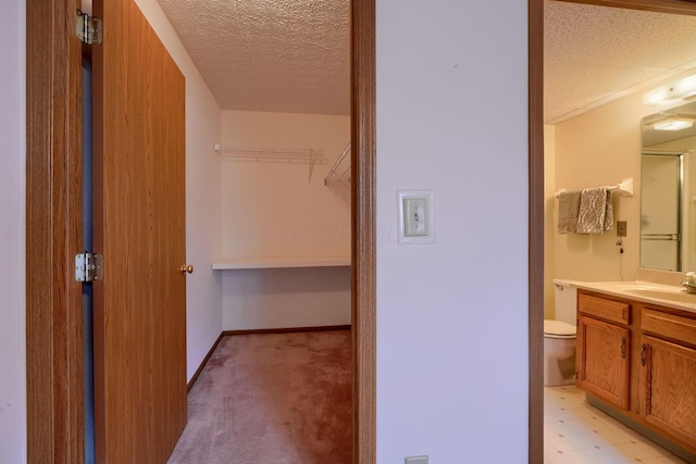 bathroom with baseboards, toilet, a walk in closet, a textured ceiling, and vanity