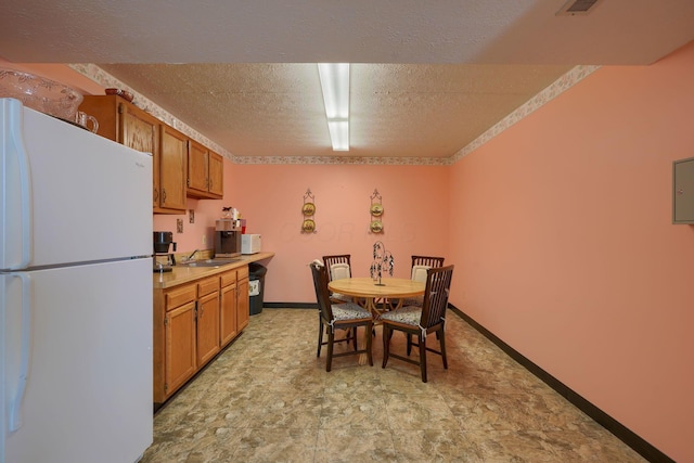 kitchen featuring freestanding refrigerator, brown cabinets, a sink, and a textured ceiling