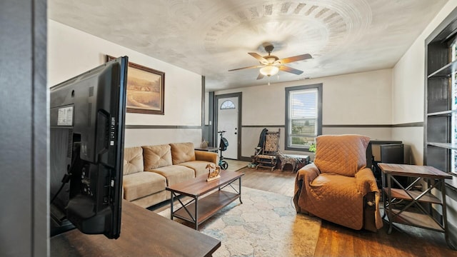 living room with a ceiling fan, a wainscoted wall, and wood finished floors