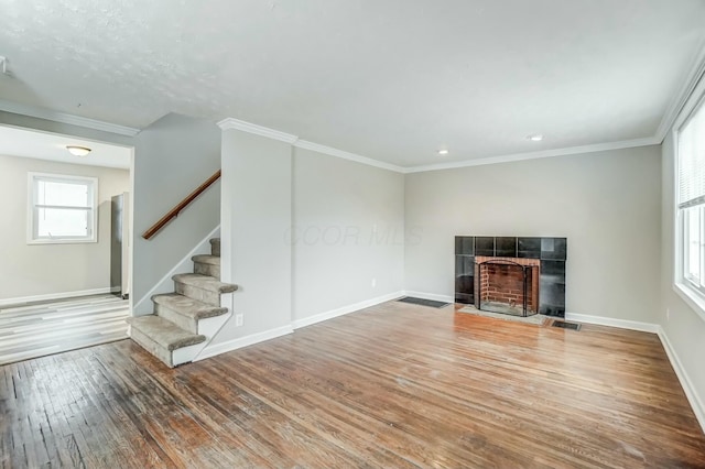 unfurnished living room featuring baseboards, visible vents, a tile fireplace, hardwood / wood-style flooring, and stairway