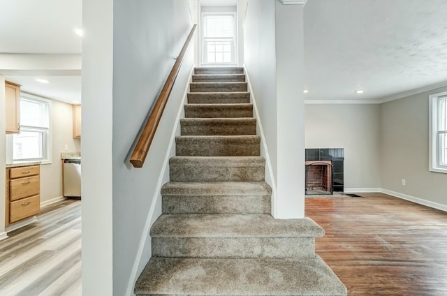 staircase with crown molding, recessed lighting, a tiled fireplace, wood finished floors, and baseboards