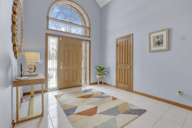 foyer entrance with a towering ceiling, baseboards, and light tile patterned floors