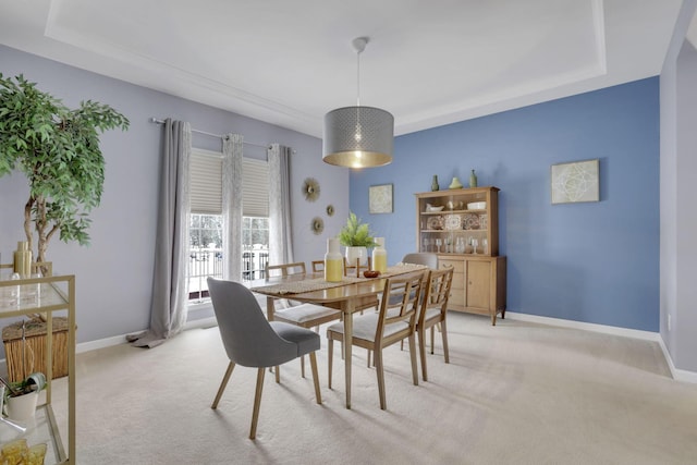 dining area featuring a raised ceiling, light colored carpet, and baseboards