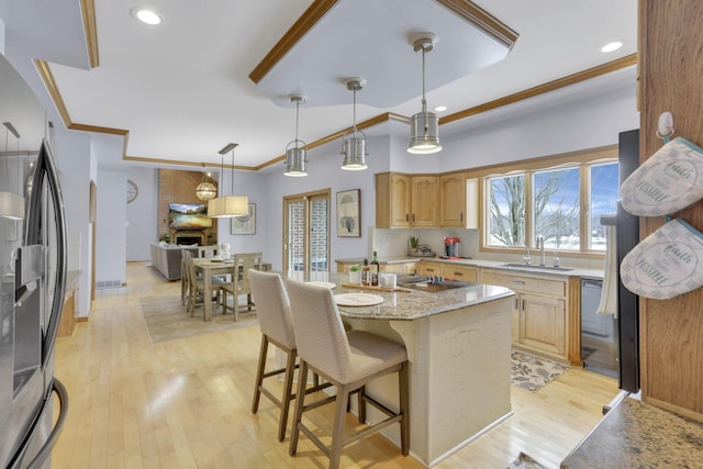 kitchen with a breakfast bar area, light wood-style flooring, a sink, stainless steel fridge, and crown molding