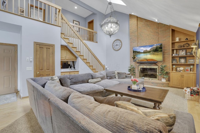 living room featuring built in shelves, a fireplace, light wood-style flooring, a chandelier, and stairs