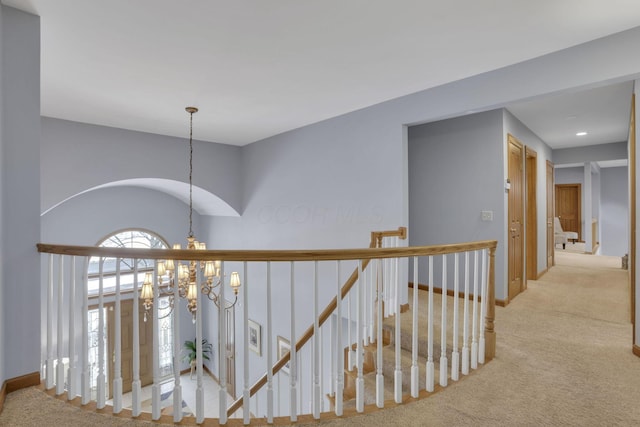 hallway featuring carpet, baseboards, a notable chandelier, and an upstairs landing