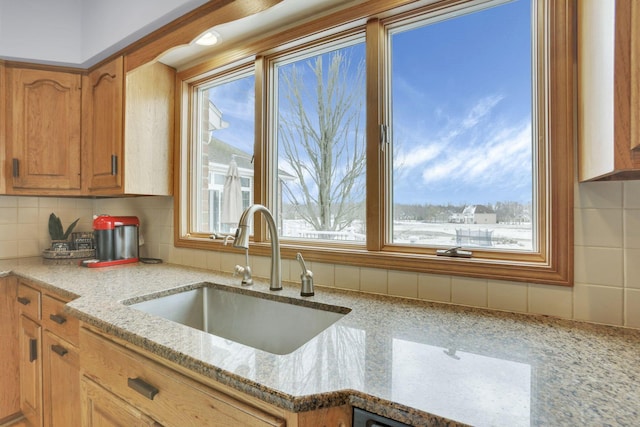 kitchen featuring brown cabinetry, a sink, decorative backsplash, and light stone countertops