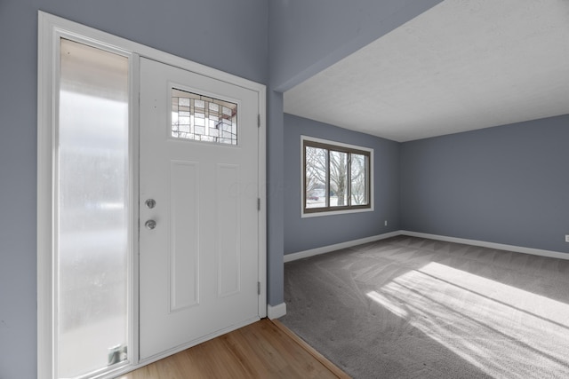 entryway featuring carpet flooring, wood finished floors, and baseboards