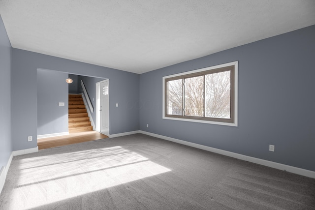 carpeted spare room featuring a textured ceiling, stairs, and baseboards