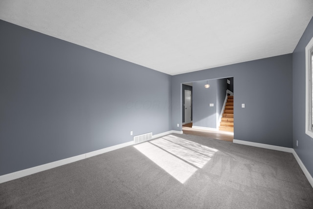 carpeted spare room featuring visible vents, stairs, and baseboards