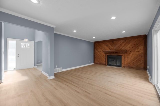 unfurnished living room with visible vents, light wood-style flooring, wood walls, crown molding, and baseboards